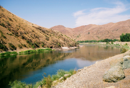 [The river abuts a tall hillside on the far side and then winds around the hill out of view. The river looks calm and the hills around it are mostly light-colored rock and dirt.]